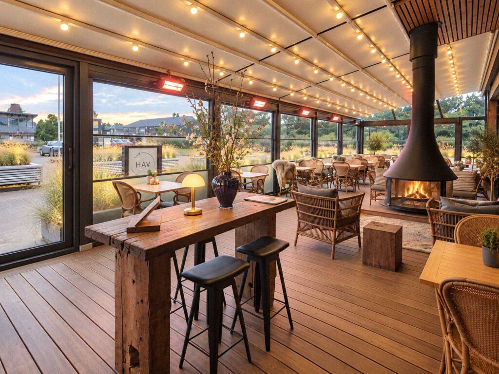 Træborde og stole under en pergola med varm belysning i restaurantens udeområde.