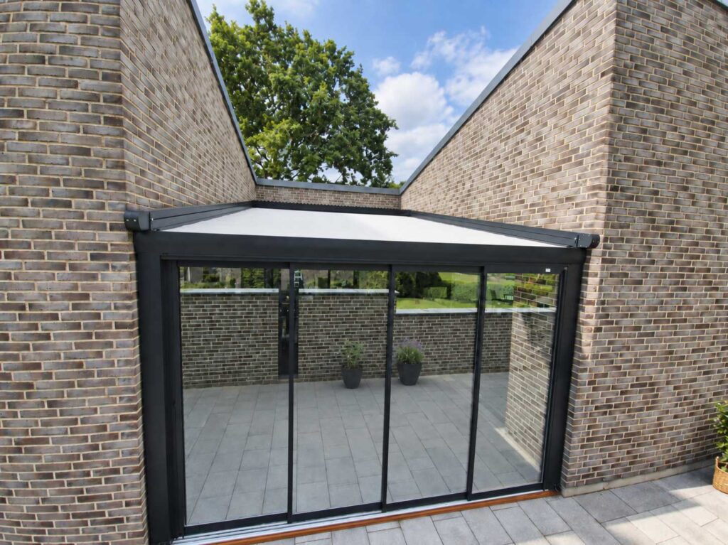 Mørk Ocean-pergola med glasfront på en terrasse mellem lyse murstensvægge.