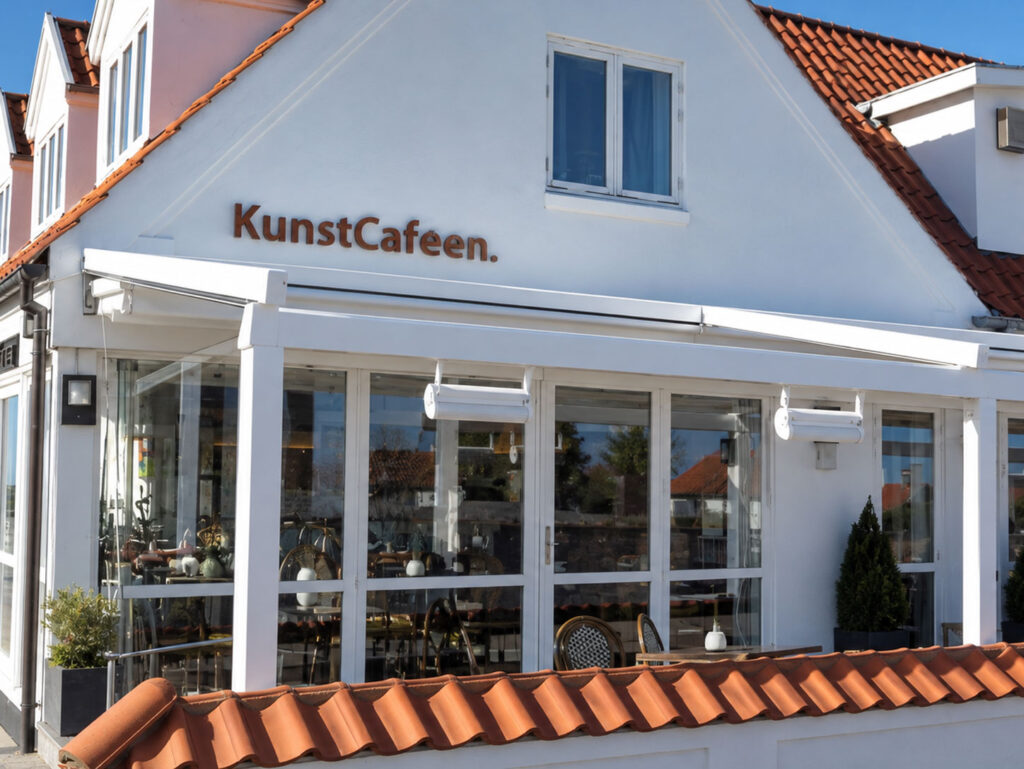 Hvid pergola foran Kunstcafeens hvide bygning med navnet på facaden.