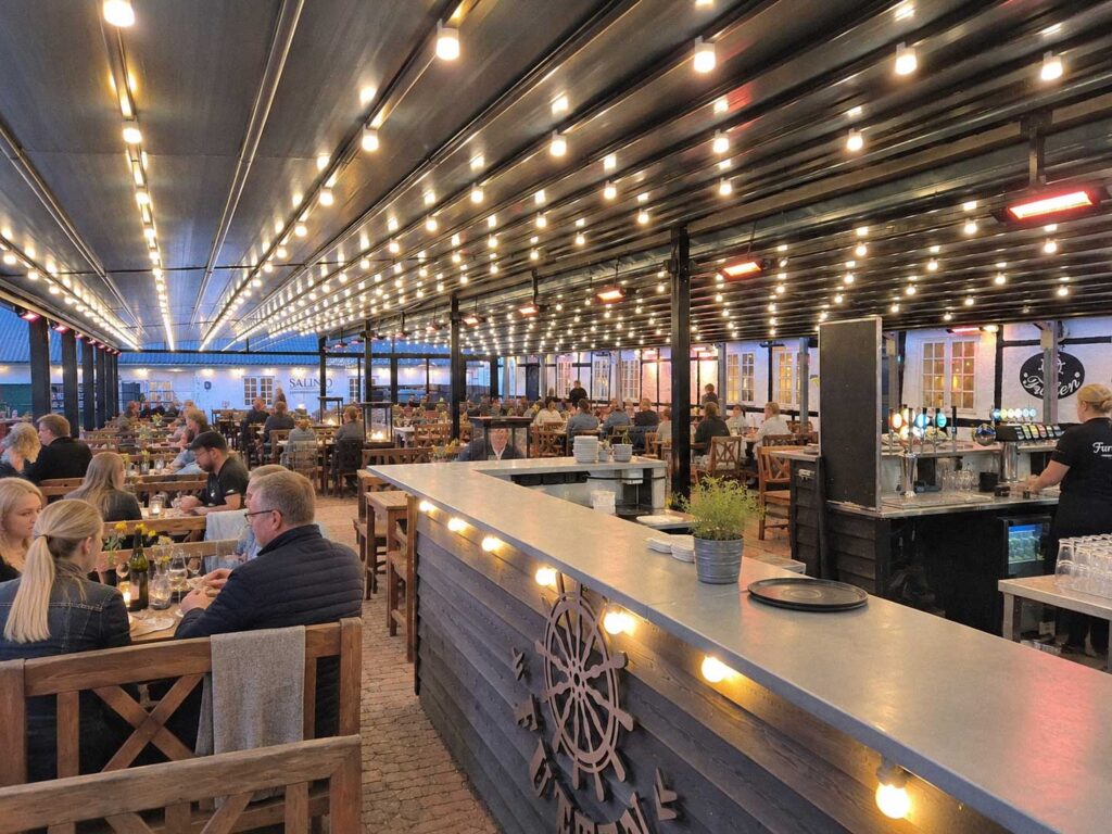 Overdækket restaurantterrasse hos Futten med borde og tændt belysning om aftenen.