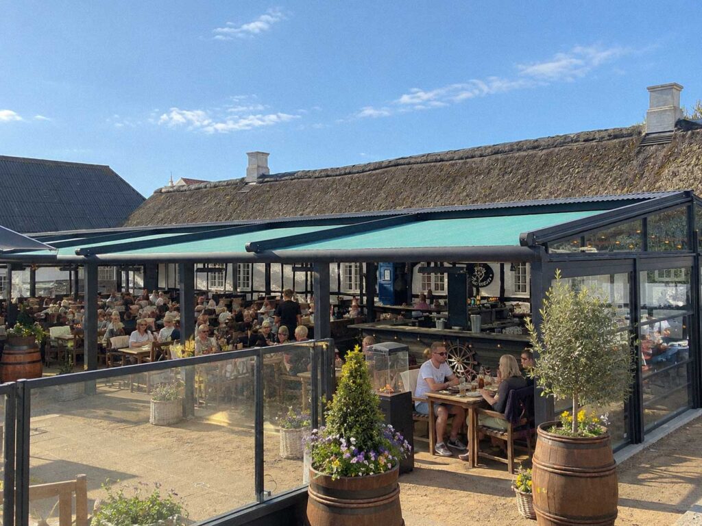 Pergola foran Futtens lange, hvide bygning, set fra udearealet i dagslys.