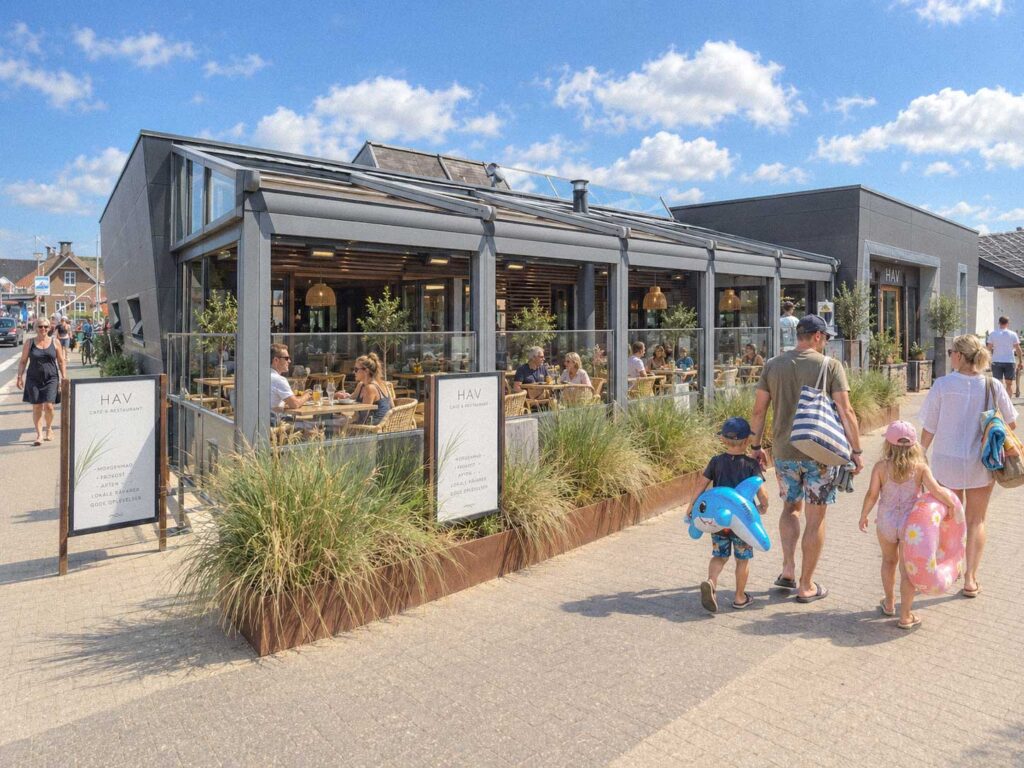 Mørk pergola med glaspartier og planter ved terrassen på Henne Strand Resort.