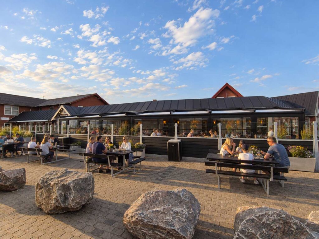 Lang overdækket terrasse foran Hvide Sande Røgeri med hvide mure og gavle i dagslys.