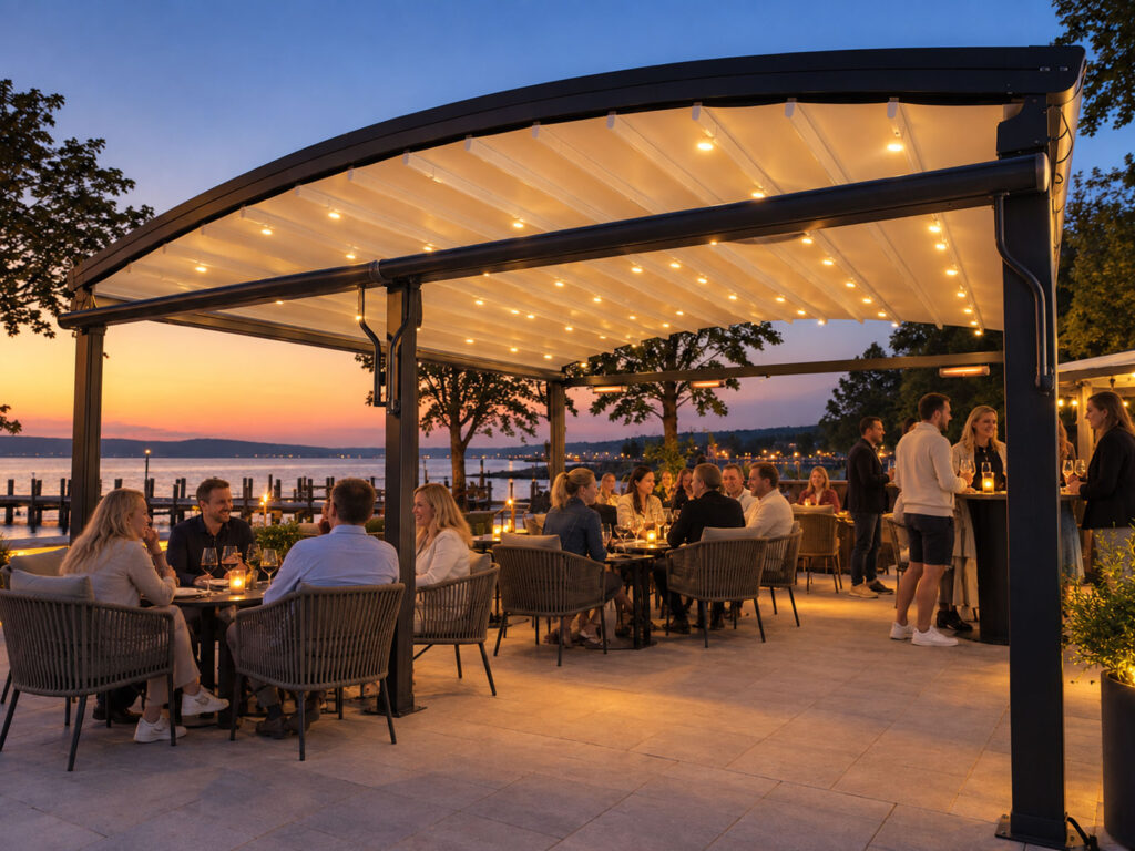 Mørk Luna-pergola over en åben restaurantterrasse ved vandet i solnedgangen.