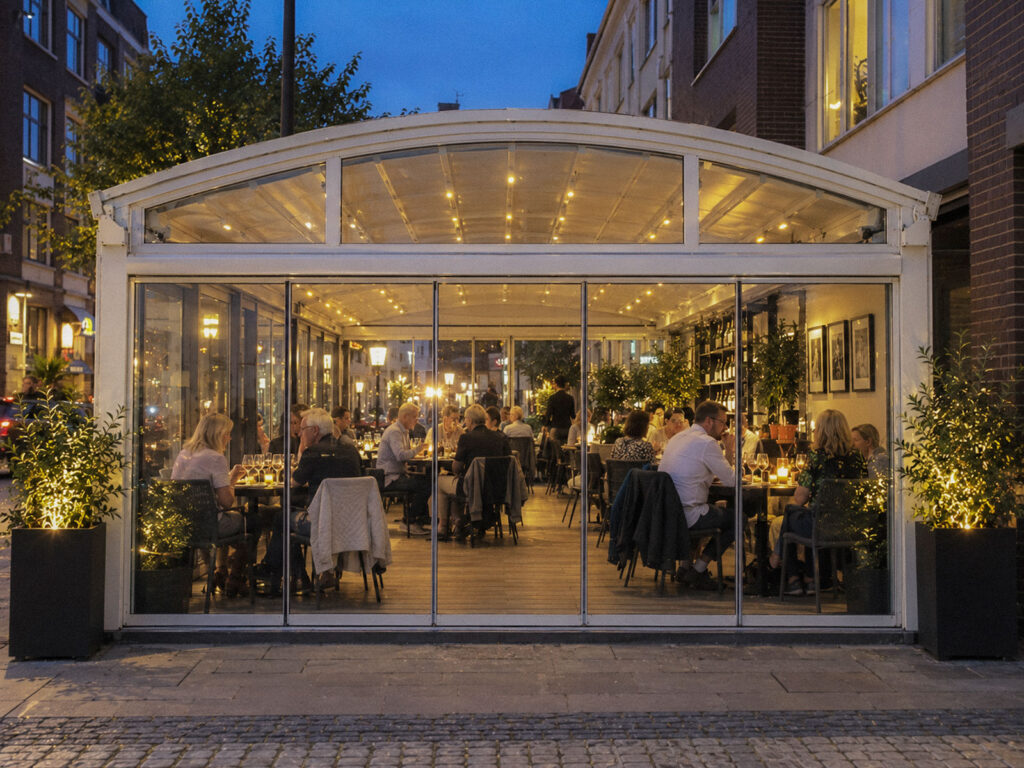 Hvid Luna-pergola med buet tagprofil og belyst glasfront om aftenen.
