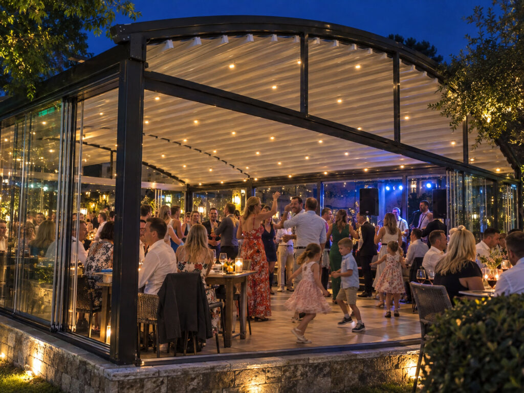 Mørk Luna-pergola med glaspartier omkring et stort selskabsområde om aftenen.