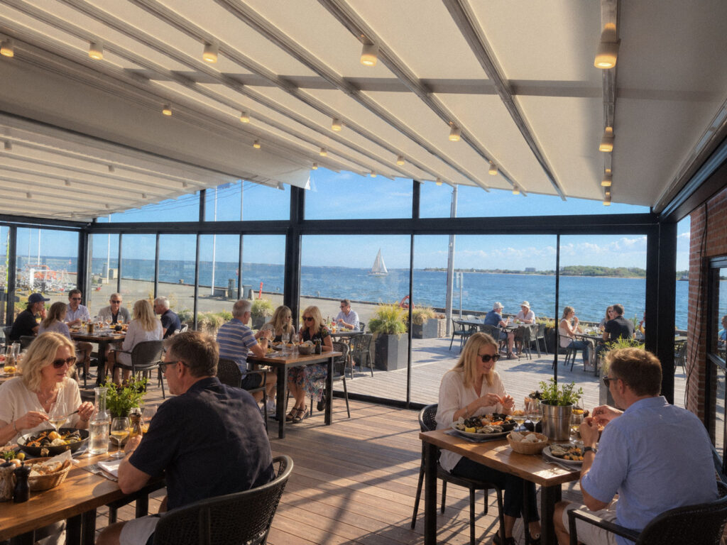 Restaurantborde under et lyst Ocean-tag med glasafskærmning og udsigt over havet.
