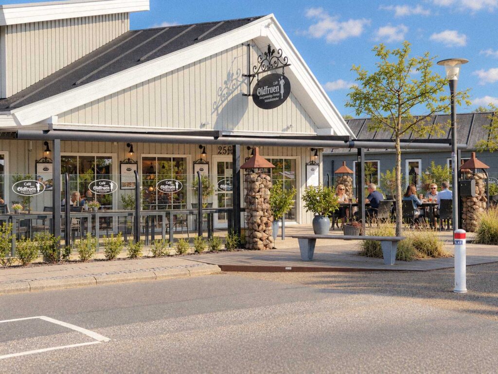 Pergola og glaspartier foran Oldfruens lyse bygning med restaurantens skilt på gavlen.