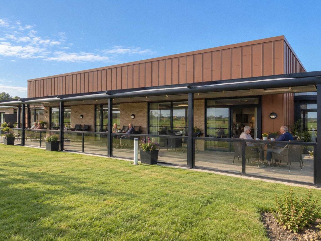 Lang terrasse med pergola og glaspartier foran et plejehjem, set fra plænen.