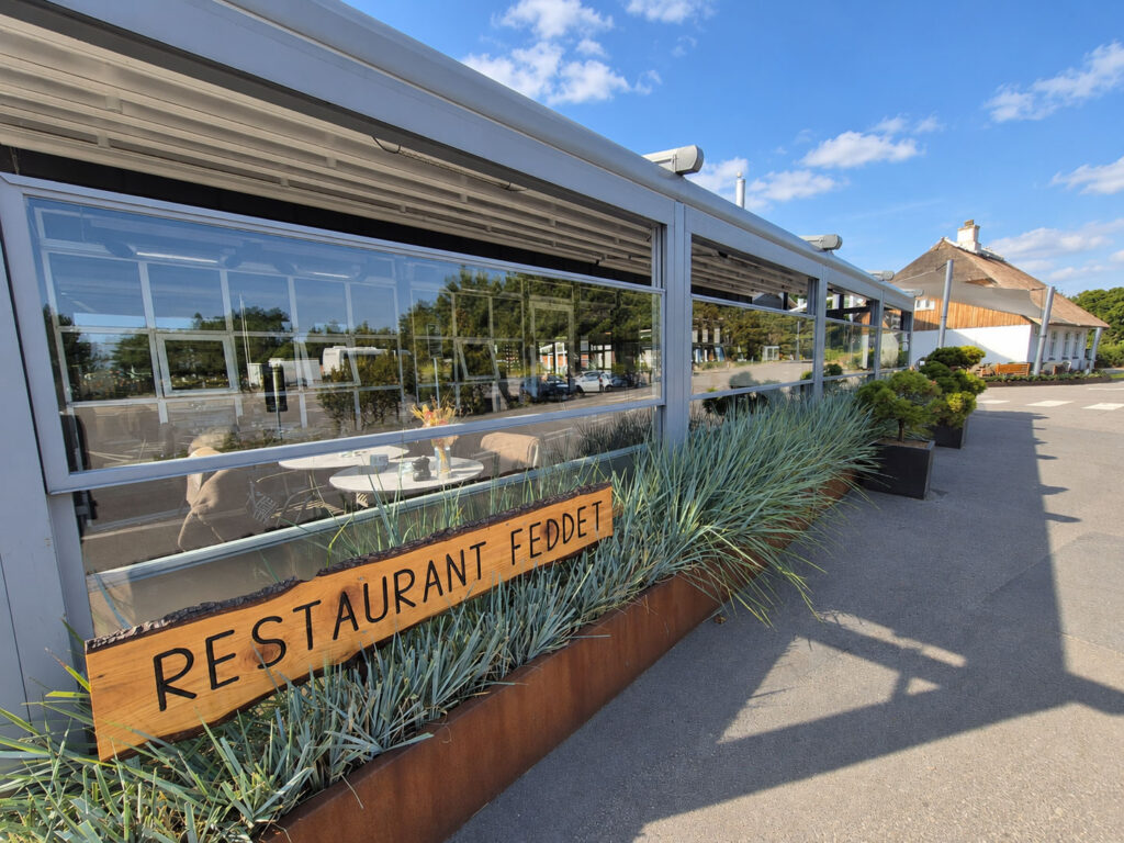 Mørk pergola med glaspartier og plantekasser foran Restaurant Feddet i dagslys.