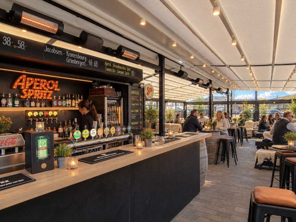 Bar med flasker i forgrunden under Strandbarens lyse terrasseoverdækning.