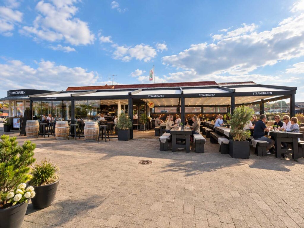 Mørk pergola med overdækket udeservering foran Strandbaren.