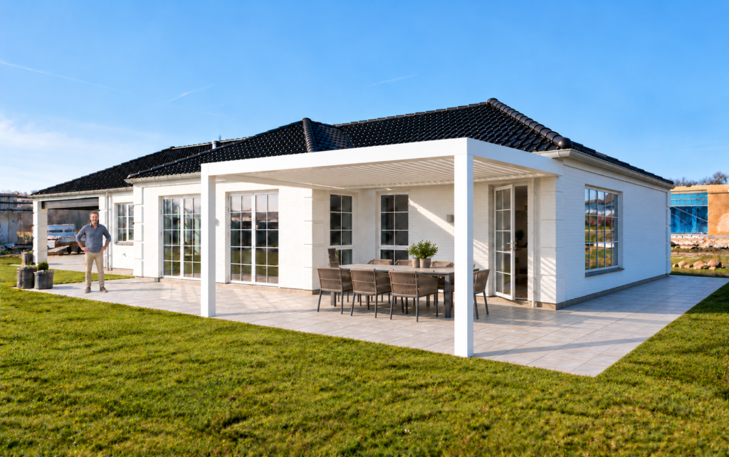 Hvid vægmonteret bioklimatisk pergola med spiseplads ved et dansk hus